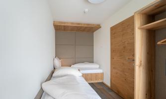 A simple room with two beds and modern design. The walls are light and the furniture is wooden.