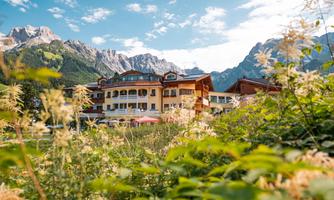 A charming hotel surrounded by green meadows and majestic mountains. The sky is clear, and nature radiates tranquility and beauty.