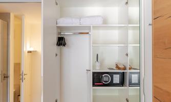 A modern wardrobe with open shelves. Inside are towels, a microwave oven, and some shoes.