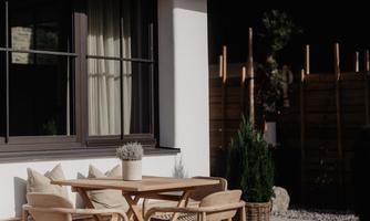 A beautiful outdoor area with a table and chairs on a wooden terrace. The environment is modern and inviting, surrounded by plants and a wooden wall.