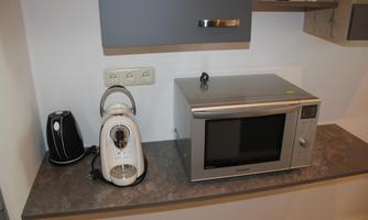 A modern kitchen corner with a microwave, a kettle, and a coffee machine. The appliances are placed on a countertop.