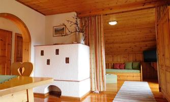 A cozy room with wooden paneling and warm colors. On the left side, there is a table and on the right side, a seating area with decorative cushions.
