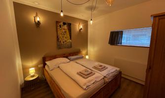 A cozy bedroom with two beds, modern lamps, and soft colors. A small window opening provides natural light.