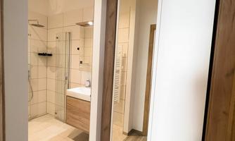 A modern bathroom with a shower and a sink. In the foreground, there is a large cabinet with a mirror.
