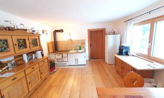 A bright kitchen with wooden cabinets and a large window. The floor is made of wood and the decor has a rustic charm.