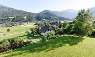 A picturesque landscape with gentle hills and green meadows. In the foreground stands a beautiful house surrounded by trees and shrubs.