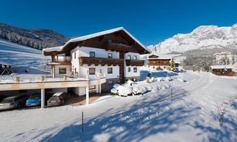 A cozy holiday home in a snow-covered landscape. The sun is shining and the mountains in the background complete the wintry scene.