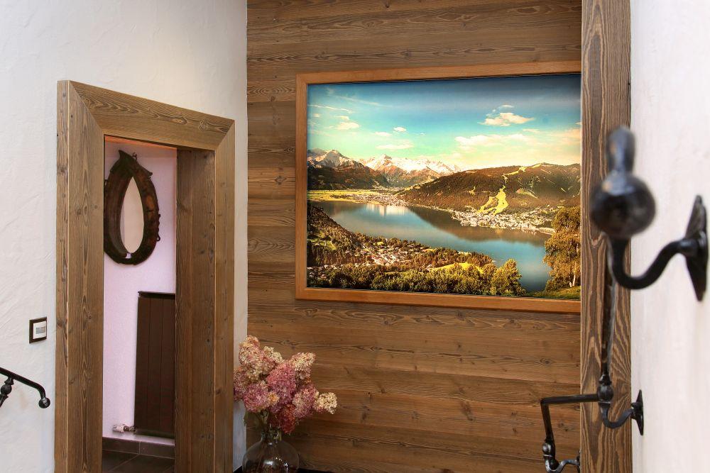 A bright hallway with wood paneling and a large landscape painting on the wall. A vase with dried flowers enhances the cozy atmosphere.