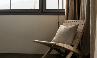 A cozy wooden armchair stands next to a window. The room has warm tones and is well-lit.