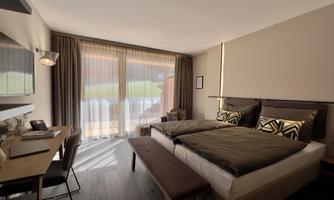 A modern bedroom with a large bed and stylish cushions. Large windows provide plenty of daylight and a view of the outdoors.