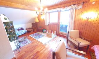 A cozy room with wooden walls and a large window. There are two armchairs, a table, and a mix of furniture and decoration.
