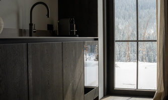 A modern kitchen with dark wood and a large window. Outside, a snowy landscape with trees can be seen.