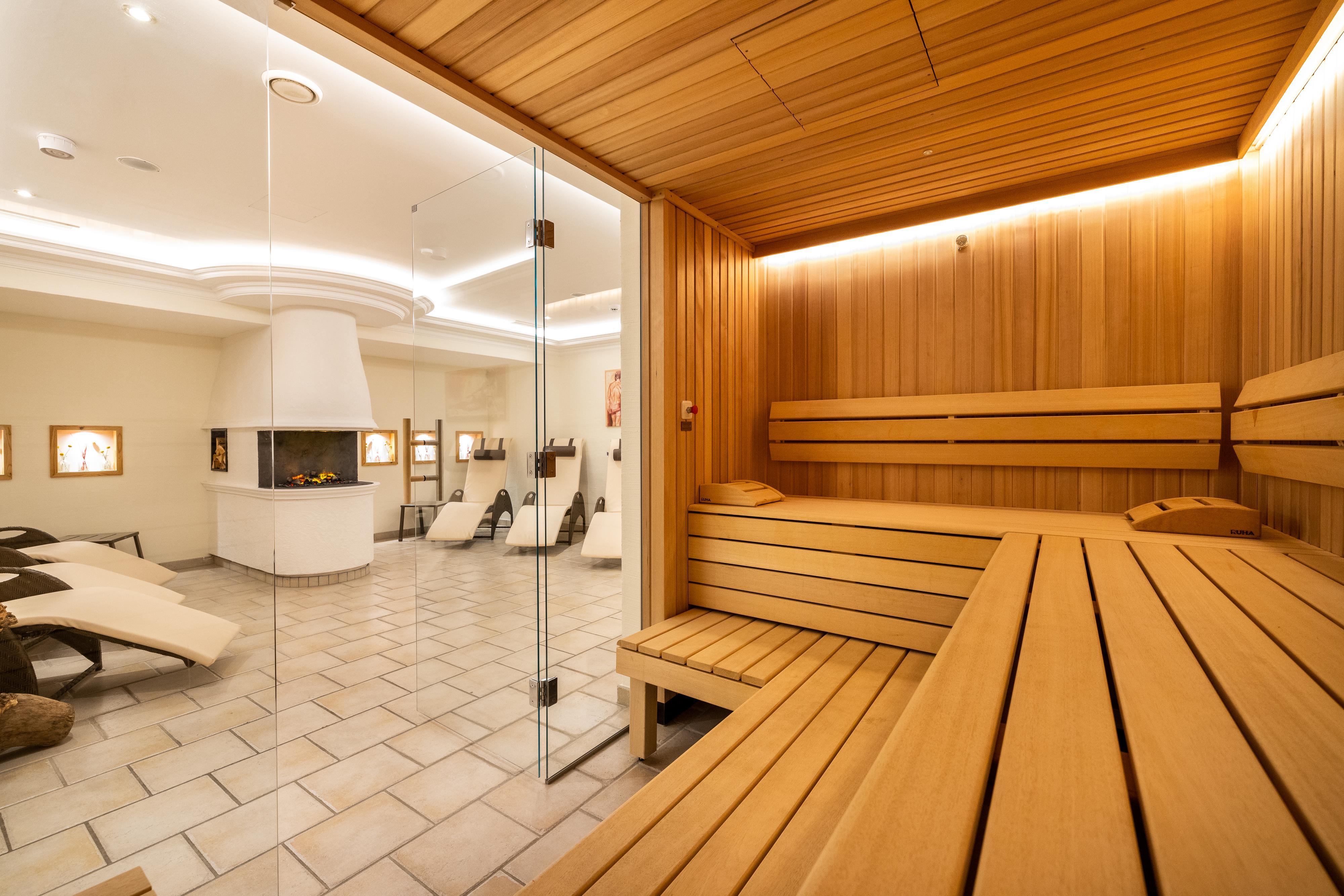 A modern wooden sauna with an inviting, warm atmosphere. In the background, relaxing loungers can be seen.