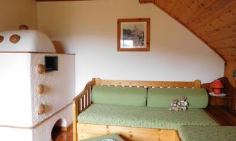 A cozy living space with a wooden ceiling and traditional furniture. There is a couch with green cushions and a stove in the corner.