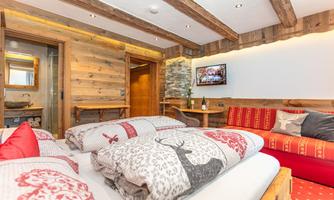A cozy bedroom with wooden decor and warm colors. A large bed with decorative blankets and a sofa create an inviting atmosphere.