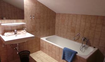 A bathroom with a bathtub and a sink. The walls are tiled and there are fresh towels.