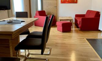 A modern living room with red furniture and wooden floor. There is a table, chairs, and a TV on the wall.
