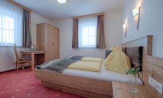 A cozy bedroom with a double bed and a desk. The bright windows and wooden furniture create an inviting atmosphere.
