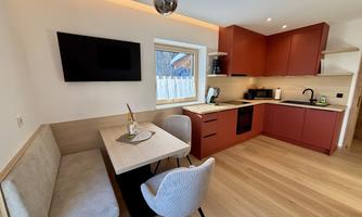 A modern kitchen with red cabinets and a wooden floor. A small dining area with a table and cozy chairs is also present.