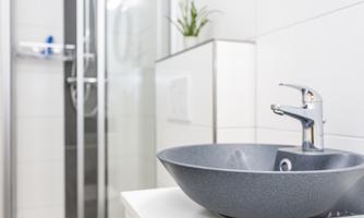 A modern bathroom with an elegant gray sink and a simple faucet. In the background, a shower cabin can be seen.