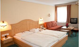 A cozy hotel room with a large double bed and a seating area. The warm wooden furniture and soft lighting create an inviting atmosphere.