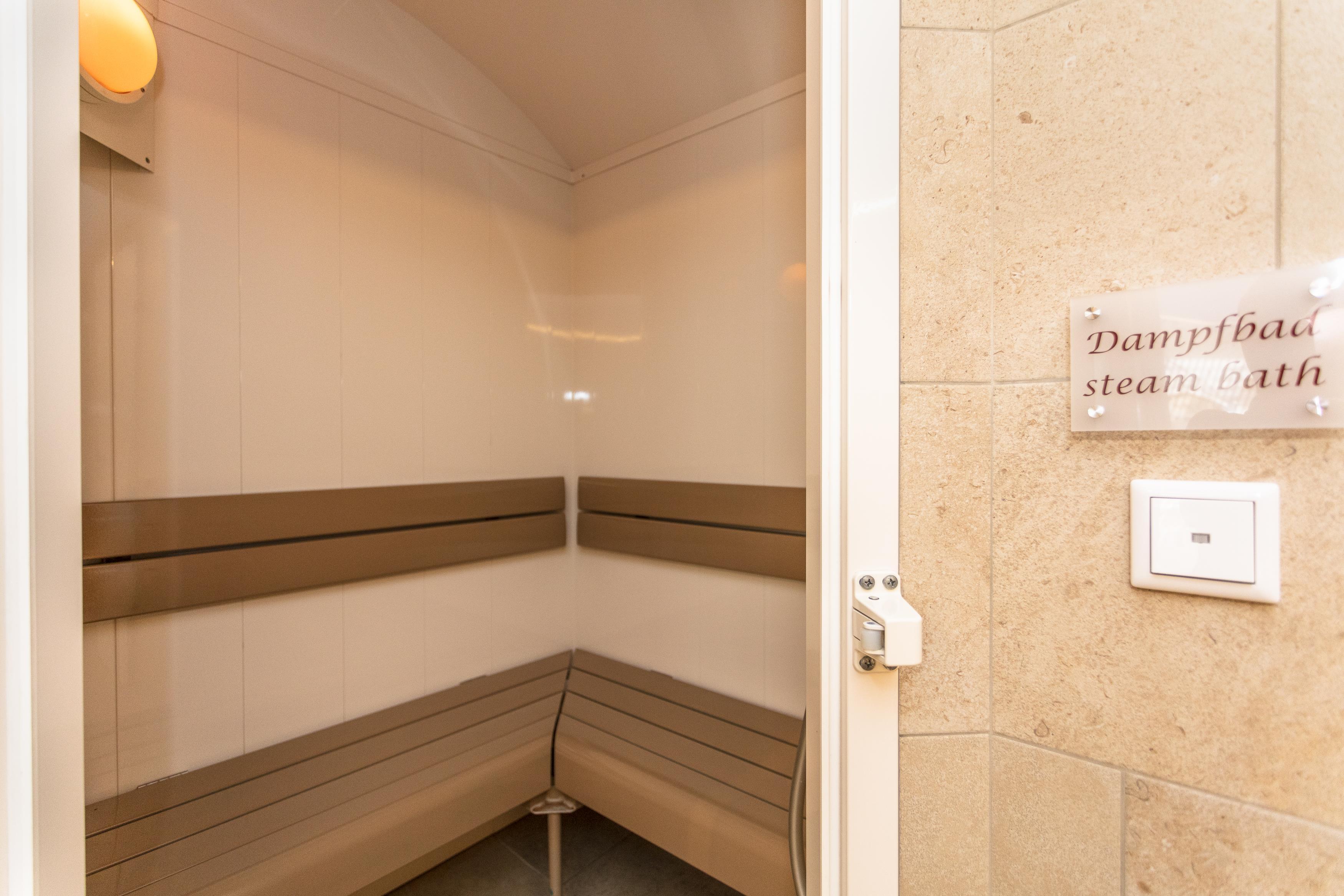 A steam bath with a wooden bench and bright walls. On the wall, there is a sign that says "Steam Bath."