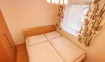 A cozy bedroom with a double bed and bright curtains. The room is well-lit and has a modern wooden wardrobe.
