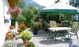A beautiful garden with colorful flowers and a cozy table under a sun umbrella. In the background, green mountains are visible.