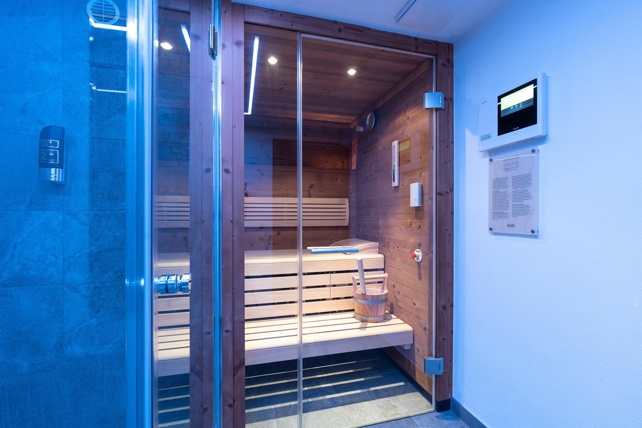 A modern sauna with a wooden bench and glass front. The lighting is soft and soothing.