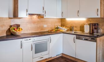 A bright, modern kitchen with white cabinets and a wood decor. On the countertop, there are fruits and kitchen appliances.