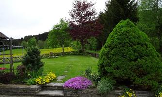A beautifully designed garden with colorful flowers and a well-maintained lawn. Surrounded by tall trees and a gentle landscape.