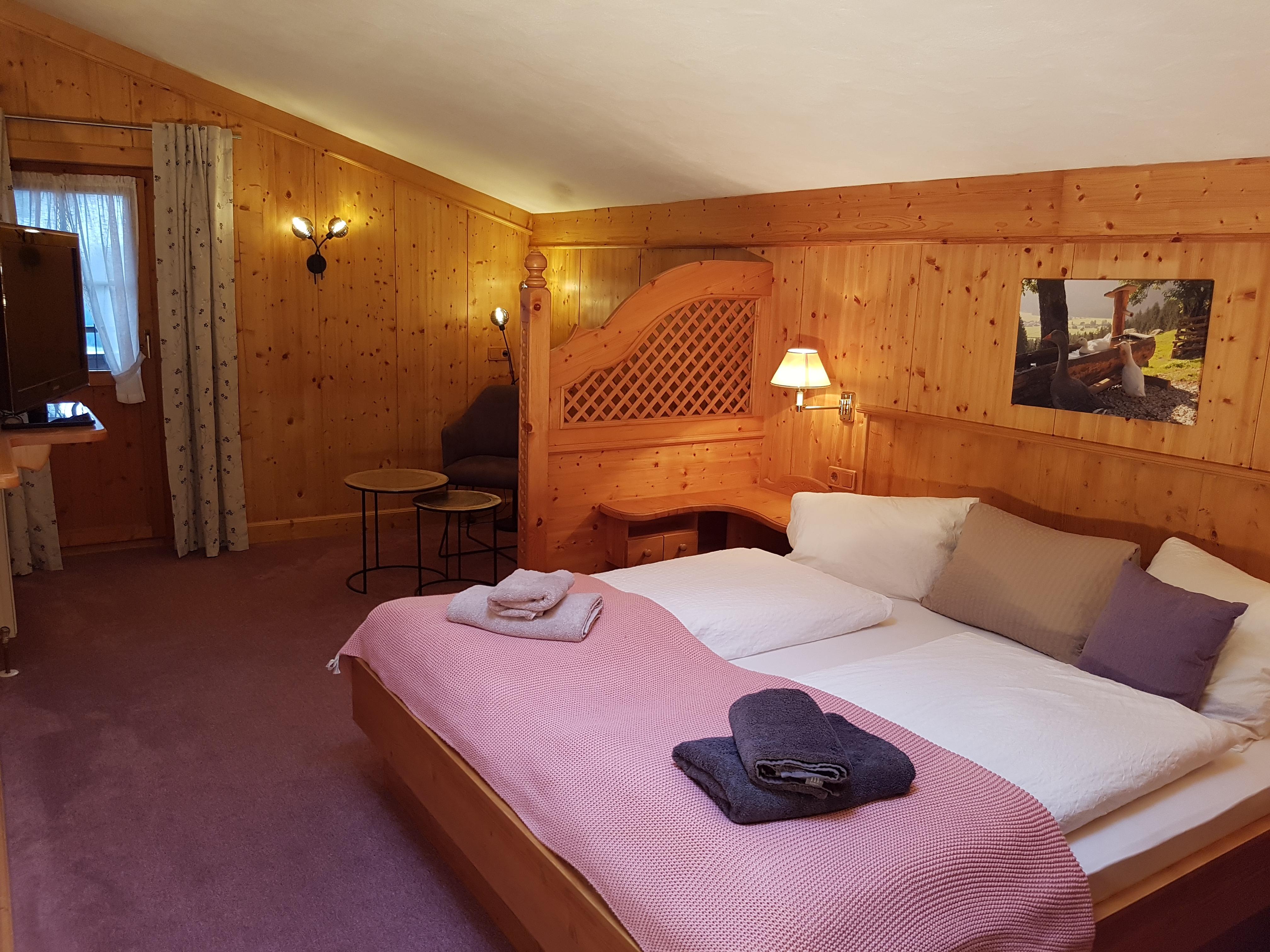 A cozy bedroom with wooden paneling and a large bed. The room is bright and inviting, with a small table and chairs.