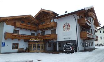 A cozy hotel in Alpine style, surrounded by snow. The facade features beautiful wooden balconies and a traditional coat of arms.