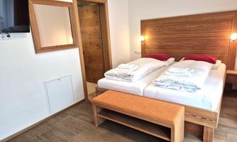 A modern hotel room with two single beds, a wooden wardrobe, and a large mirror. The walls are bright and the floor is made of wood, creating a cozy atmosphere.