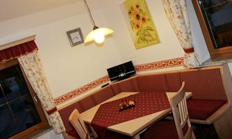 A cozy dining area with a round table and red upholstered furniture. A picture of sunflowers hangs on the wall.