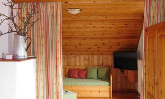 A cozy room with wood paneling, a daybed, and colorful curtains. A large TV is mounted on the wall, and a small rug is laid on the floor.