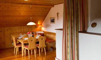 A cozy dining area with a wooden ceiling and a large table. The atmosphere is warm and inviting, with a view of beautiful wood paneling.