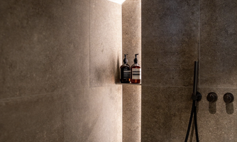 A modern shower made of gray stone with elegant toiletries on a small shelf. The lighting creates a pleasant atmosphere.