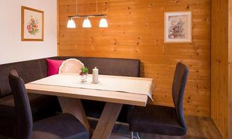 A cozy dining area with wood paneling and a modern table. The seats are upholstered in dark fabric, and a small plant adds a friendly accent.