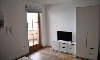 A simple room with a television, a white wardrobe, and a window with a view outside. The wooden floor and the light walls create a friendly atmosphere.
