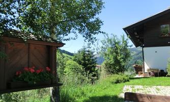 A quiet garden with a wooden bench and a flower planting. In the background, green hills and a blue sky are visible.