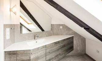 A modern bathroom with a large mirror and an elegant sink. The walls are in subdued colors and the sloping ceilings give the room a special charm.