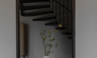 A modern staircase with open steps and gentle lighting. In the foreground stands an elegant vase with fresh flowers.