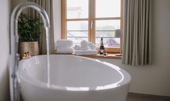 A modern bathroom with an elegant bathtub. In the background, fresh towels, a plant, and a bottle of champagne can be seen.