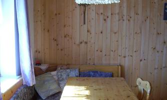 A cozy dining area with wooden walls and a round table. A hanging lamp provides soft light over the seating area.
