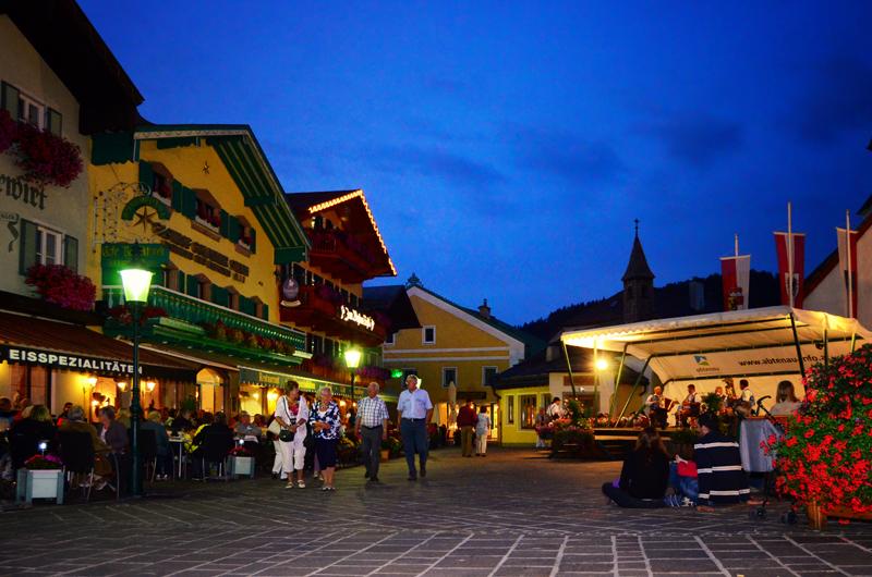 A picturesque square at dusk with cozy restaurants and people strolling. Beautiful houses with colorful windows and a festive atmosphere.