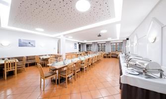A modern restaurant with many wooden tables and chairs. On the right side, there is a buffet with several warming containers.