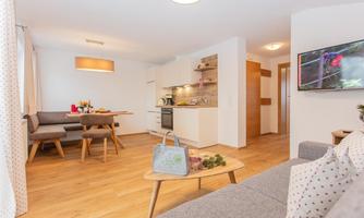 A modern kitchen with a dining table and a cozy living area. Bright colors and wooden flooring create an inviting atmosphere.