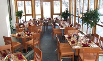An inviting restaurant with wooden tables and chairs. The tables are festively arranged and surrounded by large windows overlooking a snow-covered landscape.