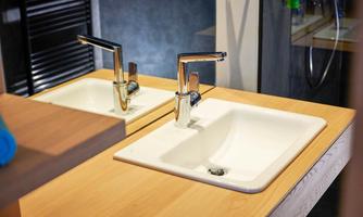 Two modern sinks on a wooden surface. The faucets are made of shiny stainless steel and give the bathroom an elegant look.